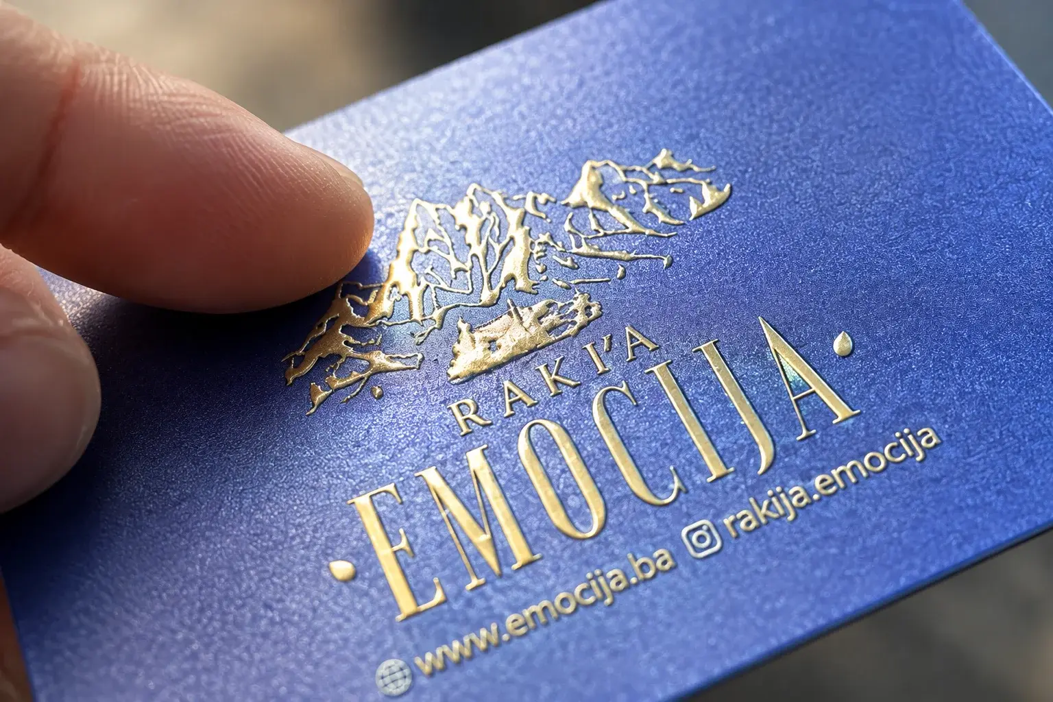 Krupni plan zlatnog logotipa na PVC vizit kartici pod kosim svjetlom, prst na reljefu