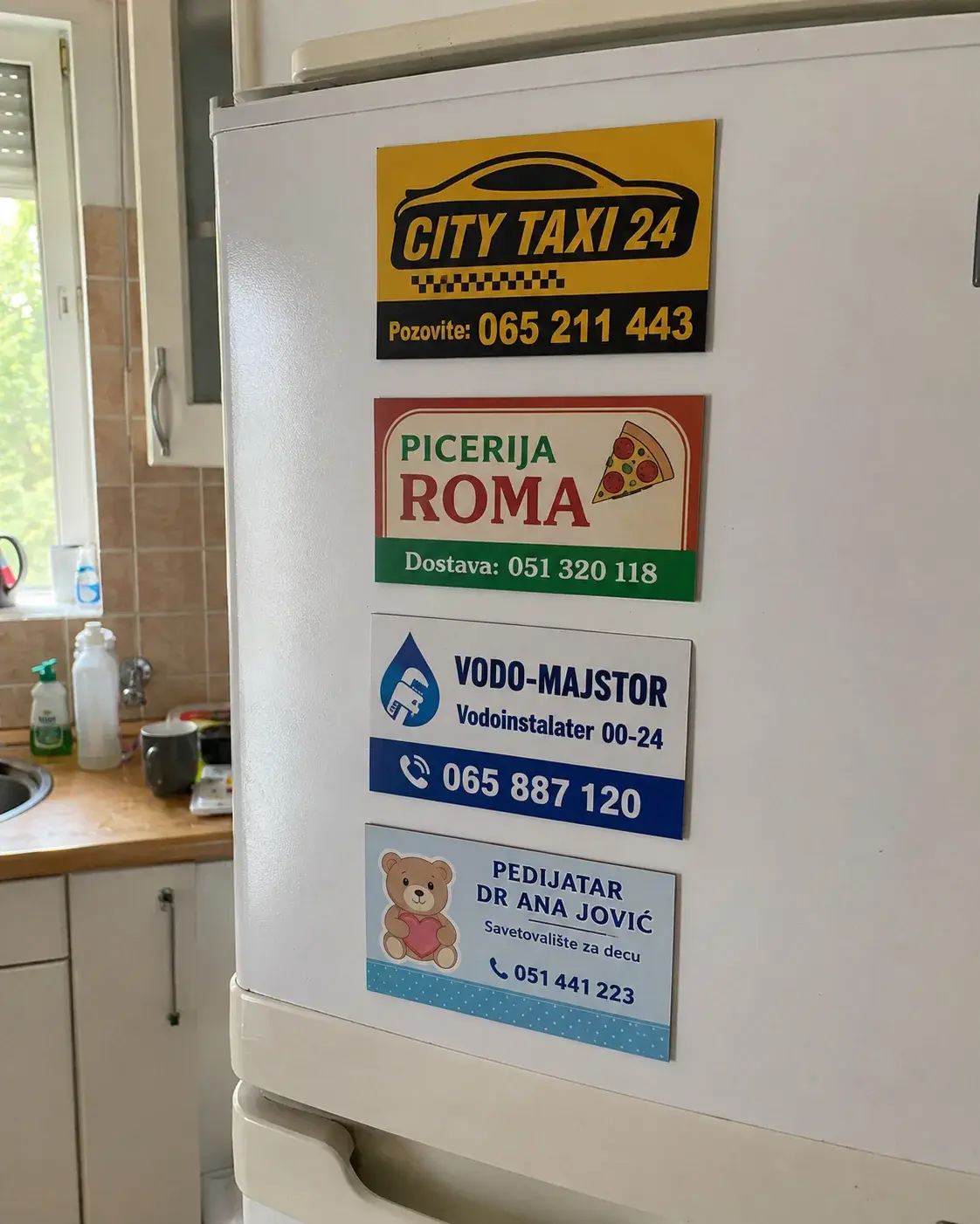 Frižider sa promotivnim magnetima različitih firmi i kontakt telefonima