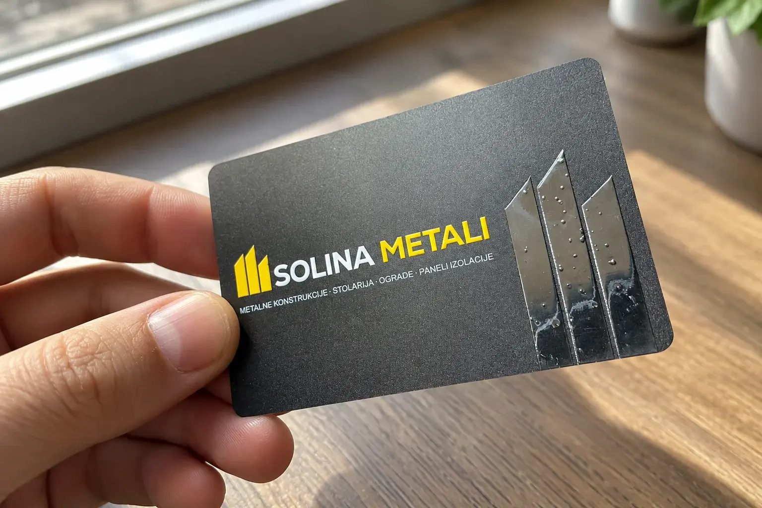Žuti logo kao sjajni reljef na crnoj mat PVC vizit kartici pod prozorskim svjetlom