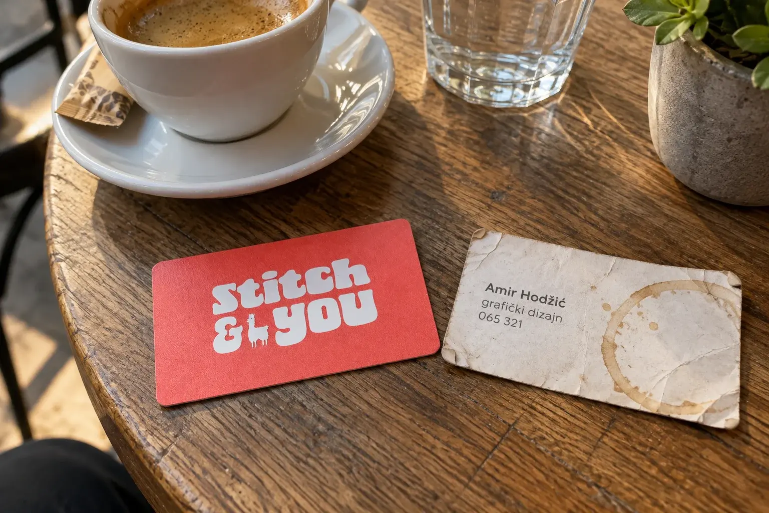 PVC vizit kartica pored iskrzane papirne vizitke sa mrljom od kafe na kafanskom stolu