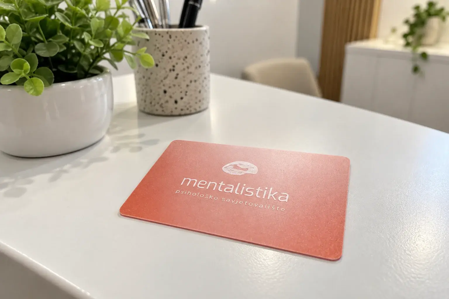 PVC vizit kartica ordinacije na bijelom pultu recepcije, biljka u pozadini