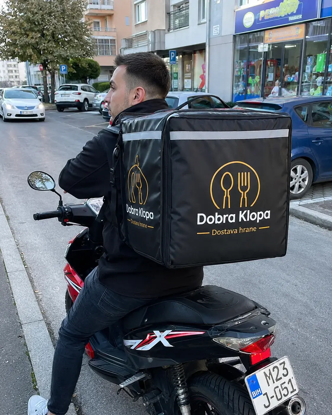 Dostavljač sa brendiranom termo torbom na motoru u gradskoj ulici