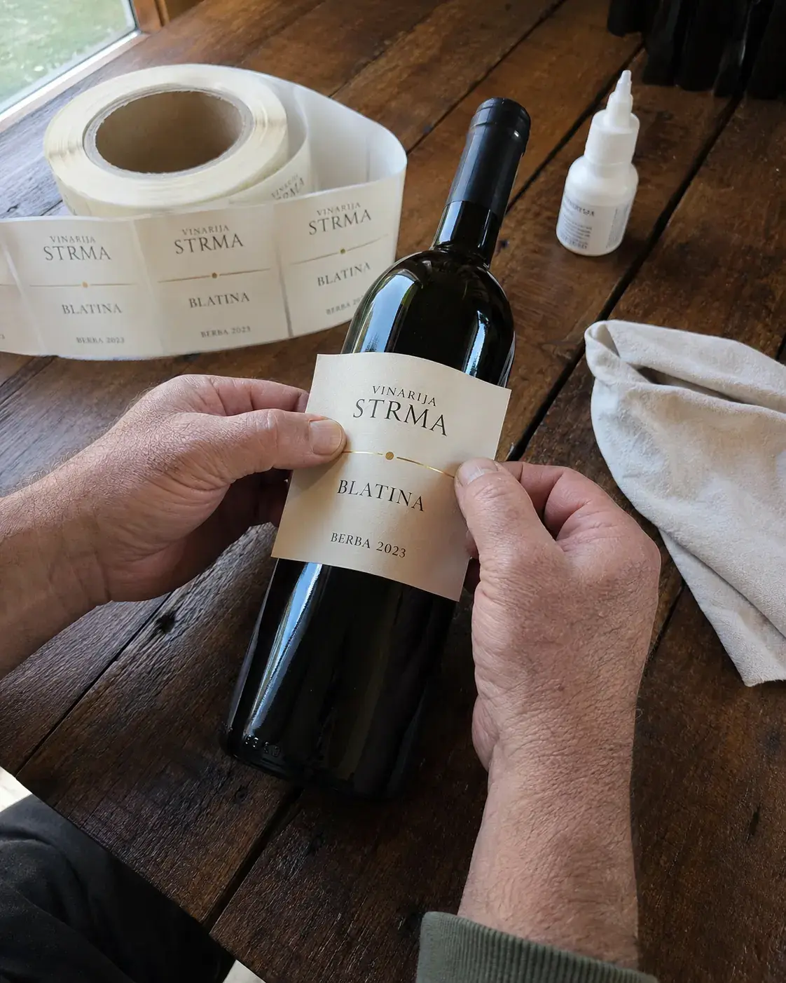 Ručno ljepljenje etikete Vinarije Strma Blatina na vinsku bocu u radionici